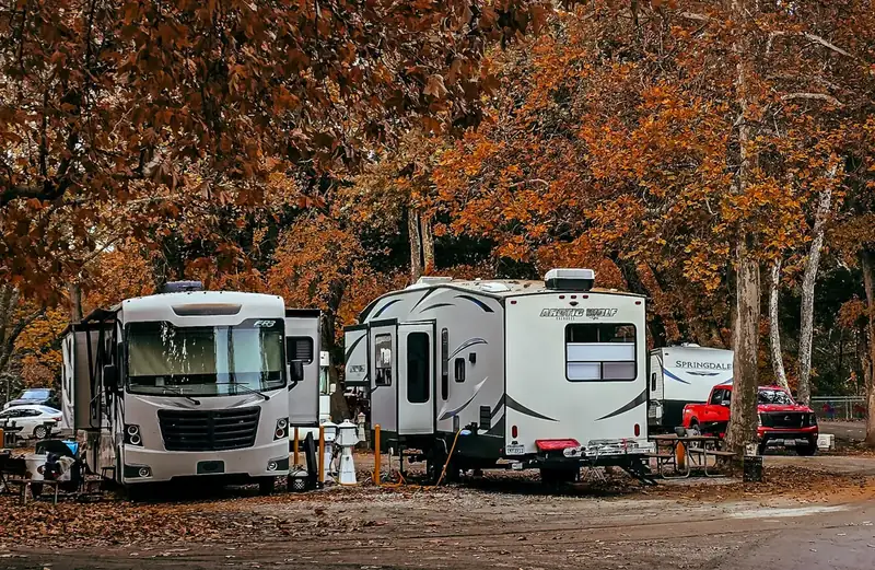 RVs parked at wooded campsites under fall color, with a pickup on the camp road