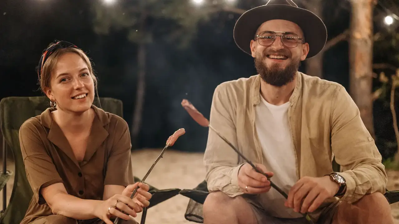 Two campers smiling while cooking over the fire on roasting sticks