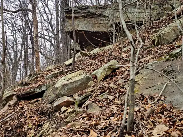 A rock overhang above a slope of loose boulders and leaves