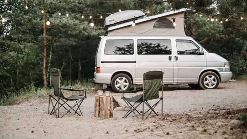 Two camp chairs and coffee mugs set out beside a camper