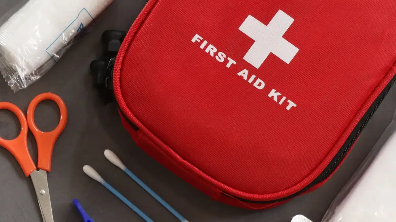 A red first aid kit with scissors, tweezers, cotton swabs, bandages and medicine