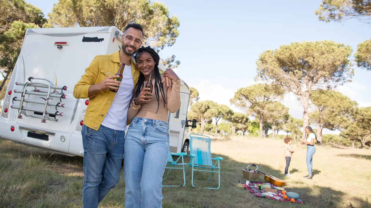 Friends relaxing beside an RV with a picnic spread on the grass