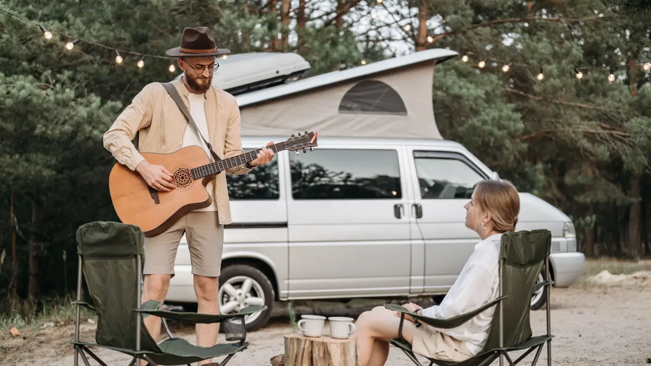 A camper playing guitar for a friend beside their van