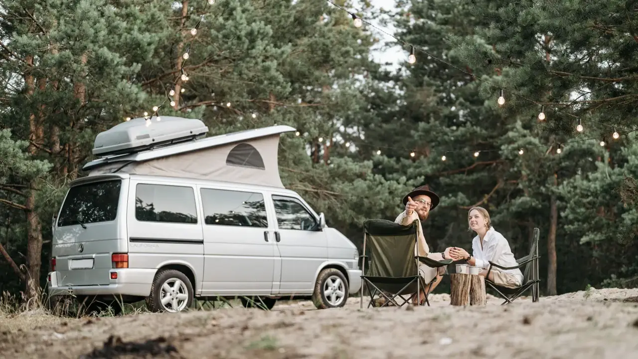 A couple relaxing by their camper van under string lights