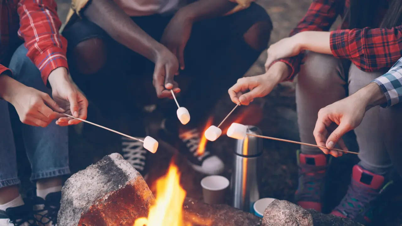 Friends toasting marshmallows over a small campfire