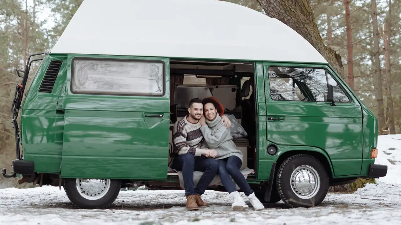 A couple in sweaters sitting in the doorway of a camper van on a snowy day