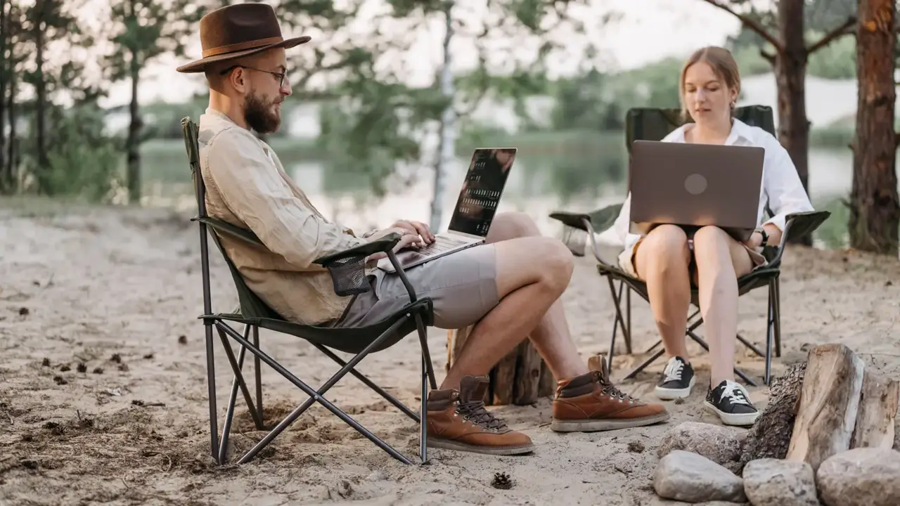 Two people working on laptops in camp chairs among the trees